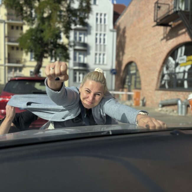 dziewczyna leżąca na masce samochodu udająca superbohatera, który leci z ręką wystawioną do przodu